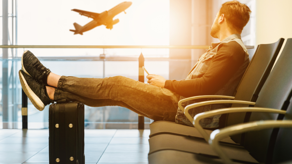 A man sitting at the airport and looking at a plane taking off.